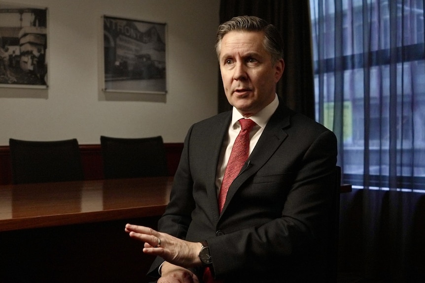 A man sits in a common room in a suit.